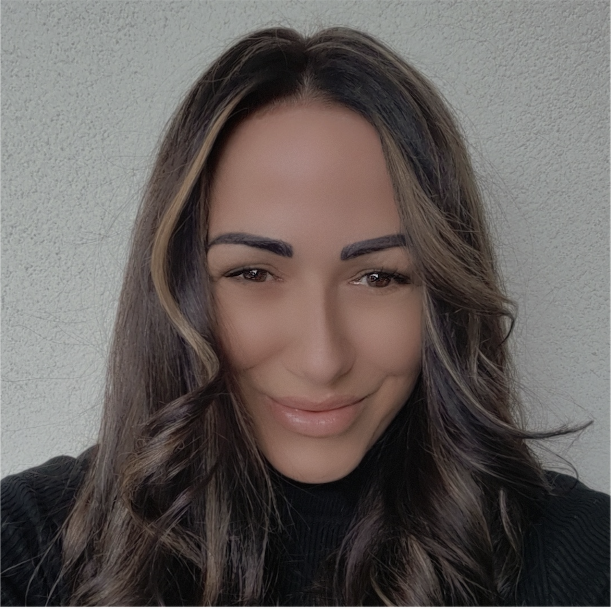 Long dark brown curly hair with subtle lighter highlights, wearing a black ribbed top against a light textured wall