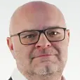 Person wearing a dark suit jacket and white shirt against a white background